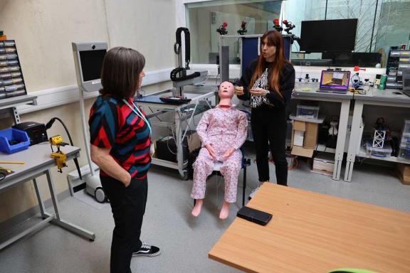 two people working with a robot with touch capabilities - the robot is designed to look like a person and is wearing pyjamas