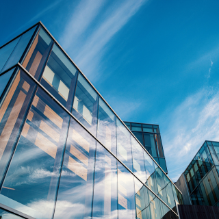 A modern glass building with a bright blue sky and wispy clouds reflected in its windows.