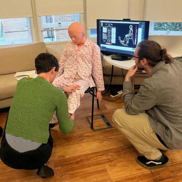 two people working with a robot with touch capabilities - the robot is designed to look like a person and is wearing pyjamas