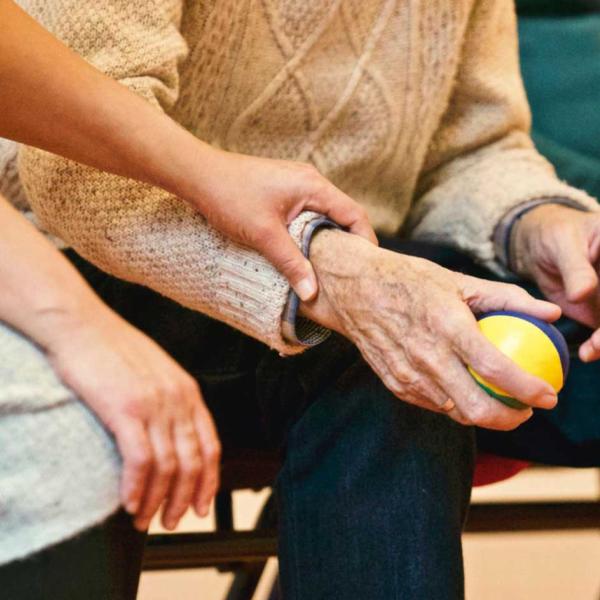 older man holding a ball, a younger woman has a caring hand on his arm